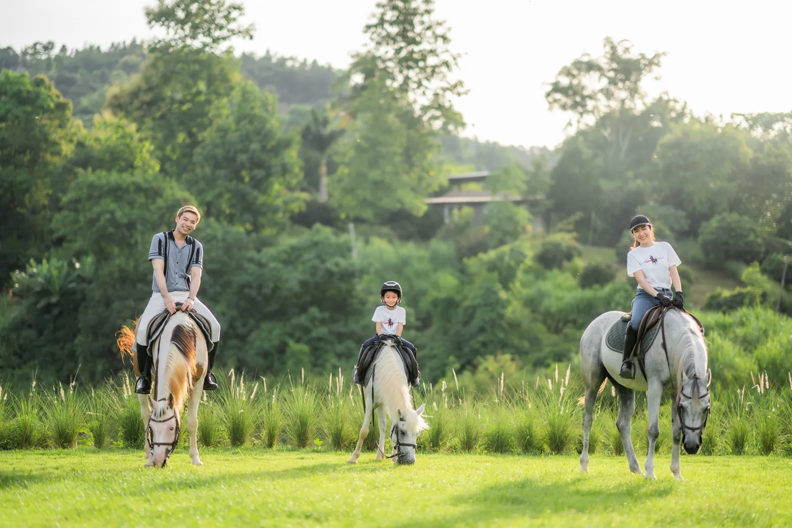 Family riding horses in a grassy field at Pong Horse Park